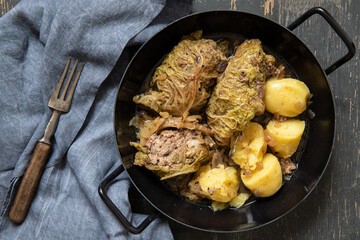 mit Hackfleisch gefüllte und Wirsing umwickelte Roulade auf dunklem Tisch aus Holz mit Kartoffeln als Beilage	