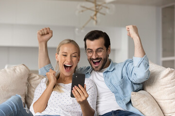 Overjoyed emotional young family couple looking at cellphone screen, feeling excited of getting...