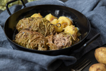 mit Hackfleisch gefüllte und Wirsing umwickelte Roulade auf dunklem Tisch aus Holz mit Kartoffeln als Beilage	