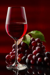 A glass of red wine and grapes on a glossy table.