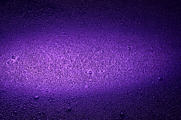 Water drops on black glass. Background illuminated with lilac ​light.
