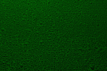 Water drops on black glass. Background illuminated with green ​light.