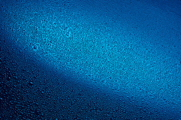 Water drops on black glass. Background illuminated with blue ​light.