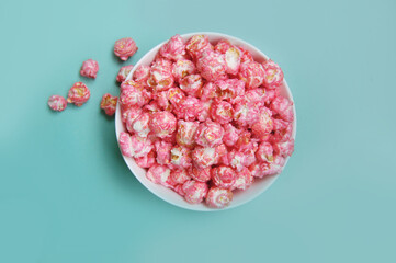 Flat lay photo of sweet pink candy (cherry, strawberry, bubble-gum) popcorn in a bowl at blue...