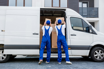 Two removal company workers unloading boxes from minibus into new home