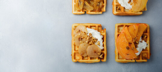 Delicious Belgian wafers with caramelized fruit, apple, banana, persimmon, pear and walnuts on a gray concrete or stone background. Ideas for breakfast. Selective focus. Top view. Place for text