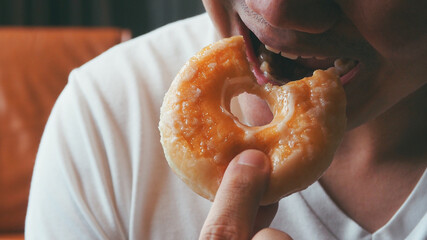 Hungry man eating and biting donut for dessert menu for unhealthy food consumption concept