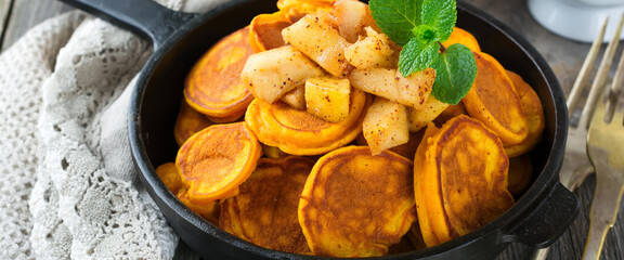 Small pumpkin pancakes with chocolate sauce in a pan on the old vintage wooden background. Selective focus