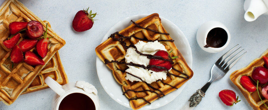 Homemade square Belgian waffles with ricotta cheese, chocolate, strawberries and cherries for breakfast on a light concrete background. Selective focus.Top view. Cope space