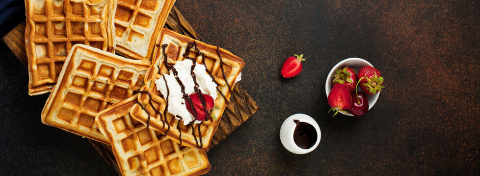 Homemade square Belgian waffles with ricotta cheese, chocolate, strawberries and cherries for breakfast on a dark background. Selective focus.Top view. Cope space