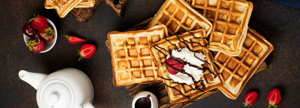 Homemade square Belgian waffles with ricotta cheese, chocolate, strawberries and cherries for breakfast on a dark background. Selective focus.Top view. Cope space