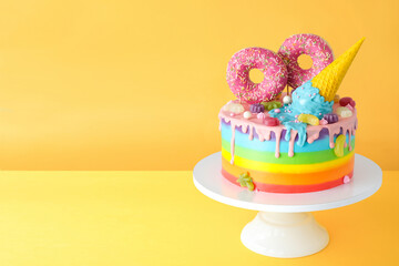 Cake on birthday with colorful rainbow cream on a yellow background decorated with berries, colorful sprinkles, poured with chocolate.