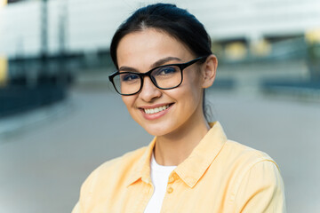 Portrait of the brunette confident woman wearing eyeglasses looking at the camera with pleasure smile while walking at the street at the fresh air. Stock photo