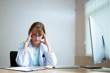 Old short blonde hair woman doctor with light blue shirt and white coat sitting on black chair in...