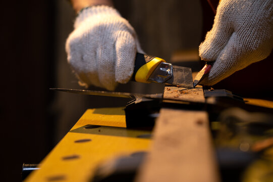 Close-up of Carpenter hands use old sharp Utility knife for manual sharpener pencil with fabric glove in warm light workshop, Using snap blade knife to sharpen pencil equipment for marking in work