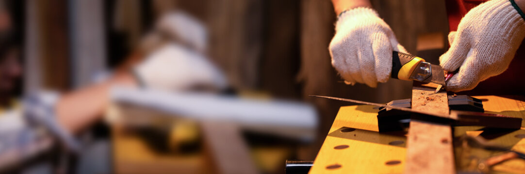 Carpenter hands use old sharp Utility knife for manual sharpener pencil with fabric glove in warm light workshop with copy space in banner, Selective focus on snap blade knife to sharpen pencil. - Powered by Adobe