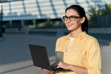 Portrait of positive joyful brunette woman standing with her laptop and smiling while looking away. People and technologies concept