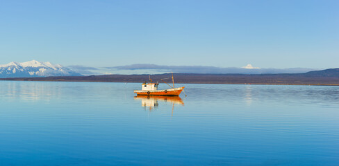Fjord with small fishing boat and snow covered mountains in south Chile
