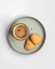 A cup of coffee and two heart shaped cookies in a plate, top view