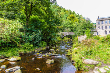 A view along Hebden Beck towards a bridge and old mill on the outskirts of Hebden Bridge, Yorkshire, UK in summertime