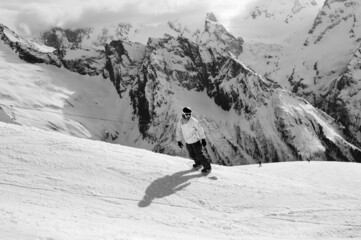 Snowboarder downhill on ski slope in high snowy mountains. Black and white toned