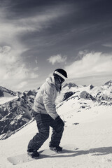 Fototapeta na wymiar Snowboarder downhill on snowy ski slope in high mountains. Black and white retro toned image.