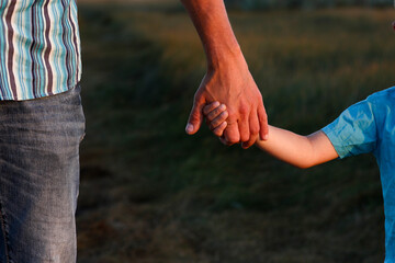 A Hands of a happy child and parent in nature in a park by the road