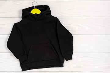 Black fashionable kid sweatshirt with a hood with clothes hanger on white background top view....