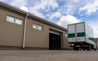 Naklejka premium A truck drove up to a building with an open gate for loading and transporting cargo. Production logistics.