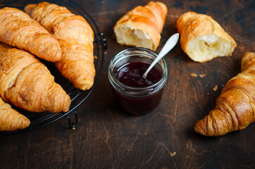 Freshly baked croissants with jam on dark wooden background.