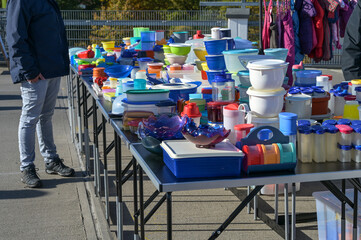 Lots of colorful plastic storage containers and tubs on tables at a garage sale or flea market...