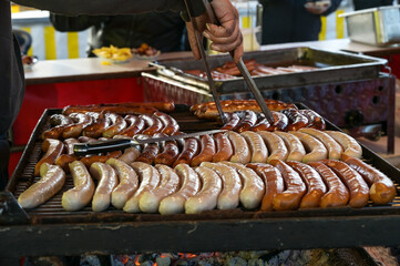 Man with dirty hands turns sausages with tongs on a street grill, typical food on a German county...