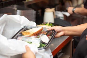 A view of an employee preparing to pack a food to-go container, in a restaurant kitchen setting.
