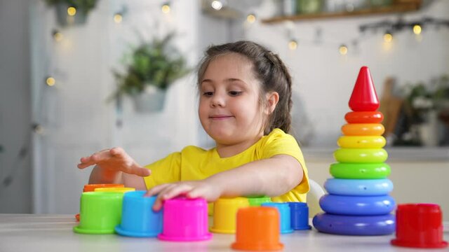 Happy girl at table.Child plays with colored toys at table. Girl in room at home. Child building house. Girl with colorful toys at table. Children's room preschool education.Little kid playing at home