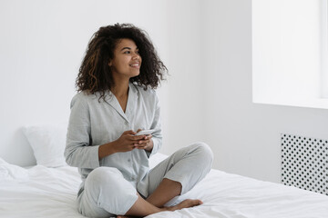 African american woman sitting with smartphone on bed