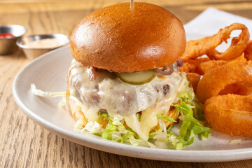 A closeup view of a thick cheeseburger, with a side of onion rings.