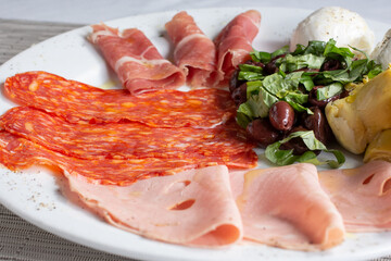 A view of a platter of antipasto, featuring cured cold cuts, olive salad, and mozzarella cheese.