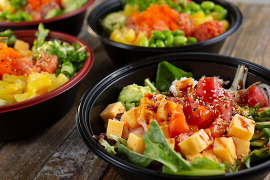 A closeup view of several customized poke bowls on a wooden table surface.