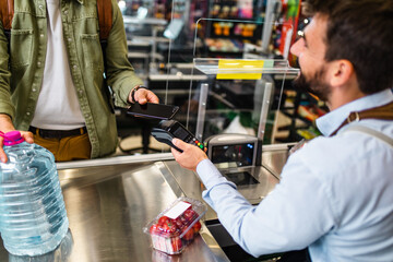 Man buing fresh vegetables and water at grocery store. Contactless payment by mobile phone.