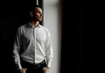 Fototapeta premium young man in white shirt stares to the left side of the window