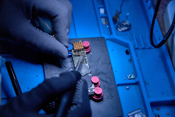 Hands in gloves of cellphone technology maintenance engineer work on chipset pins of removed microprocessor from smartphone motherboard with soldering iron. Close-up macro photo, Selective focus