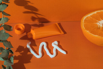 A tube of cream, an orange, squeezed cream and leaves on an orange background.