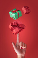 Gifts wrapped in colorful paper flying on a female hand on a red background, Christmas and holiday concept.