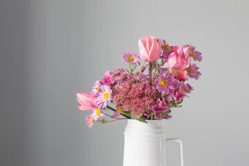 pink flowers in white jug on background gray wall