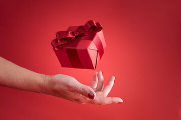 Female hand with flying gift on red background, Christmas and holiday greetings concept.