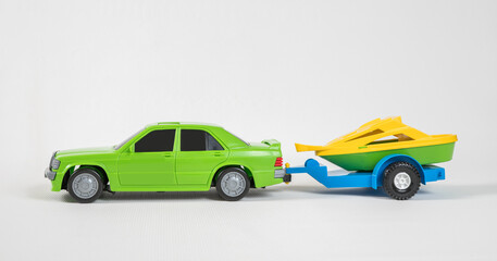 Trailer for transporting a motor boat. Plastic toy multicolored cars isolated on white background. A car with a motor boat on a trailer.