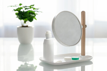 Contact lens accessories on a white table. Table mirror, contact lens container, solution.
