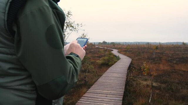 Unrecognizable man in wilderness surrounding is trying to determine his location using a mobile map app on his smartphone. Lost in willdernerss concept. 