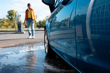 portrait young, smiling, happy, attractive woman washing automobile at manual car washing self service station, cleaning with foam, pressured water. Transportation, auto, vehicle care concept