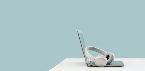 Laptop. Mockup screen and wireless headphones on white desk. plain blue background. Distant learning. working from home, online courses. minimal. Helpdesk support or call center headset